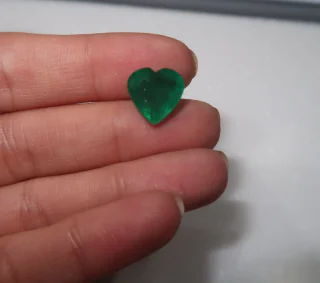 A heart cut emerald held between two fingers in daylight